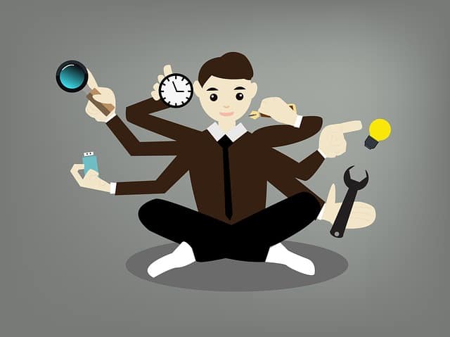 A businessman multitasking with multiple arms holding a clock, a magnifying glass, a USB stick, a pen, a lightbulb and a spanner
